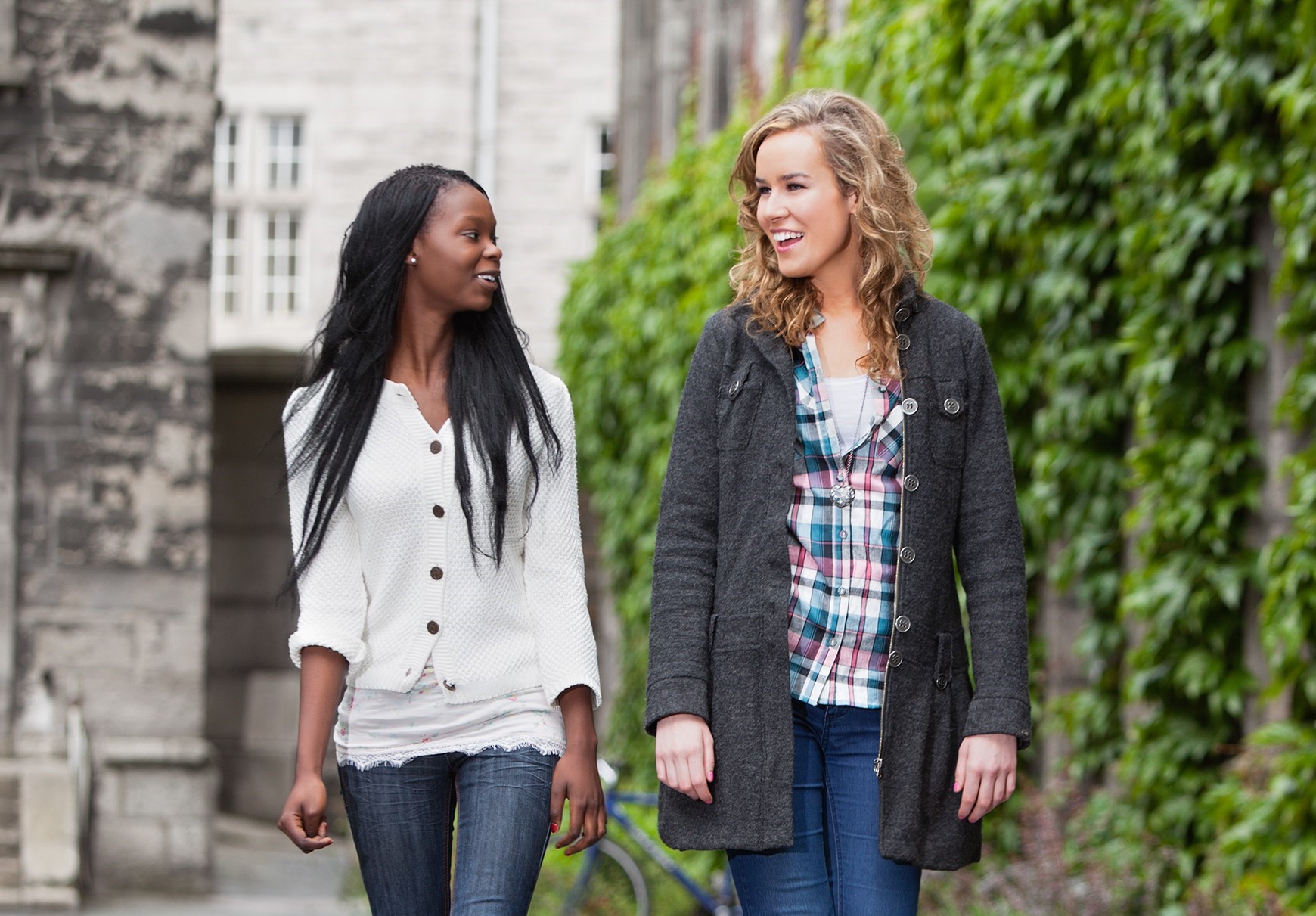 Young black woman and whte woman wlak and talk together on college campus